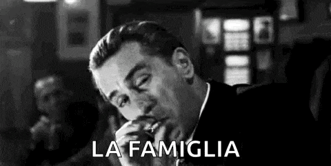 a man is smoking a cigarette in a black and white photo with the words `` la famiglia '' written above him .