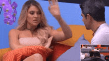 a man and a woman are sitting on a couch and the woman is waving her hand .