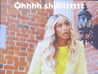 a woman in a yellow jacket is standing in front of a brick wall and says ohhhh shiiiittttt .