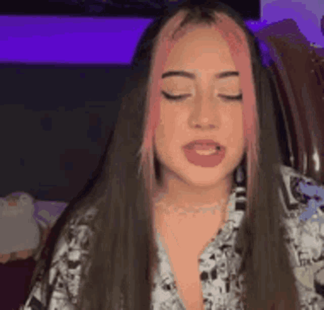 a woman with long hair and pink streaks is sitting in a chair with her eyes closed and her mouth open .