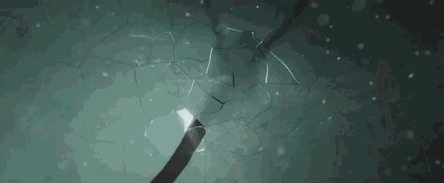a person is breaking a glass wall with a hammer and a light coming out of it .