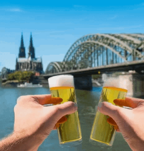 two glasses of beer are being toasted in front of a bridge