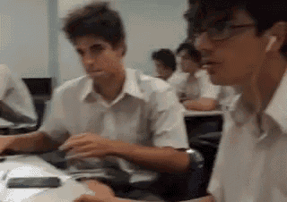 a group of young men are sitting at desks in a classroom looking at a computer screen .