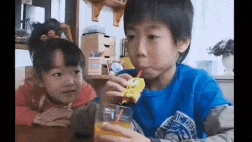 a boy and a girl are drinking orange juice through a straw .