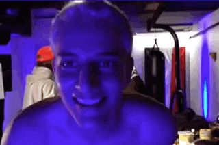 a man without a shirt is smiling in a dark room with blue lights .