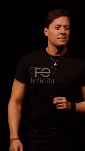 a man wearing a black shirt and a cross necklace is singing