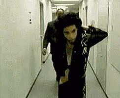 a man in a black jacket is walking down a hallway with a man in a suit .