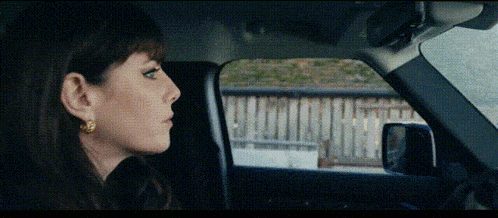 a woman wearing gold earrings is sitting in a car looking out the window
