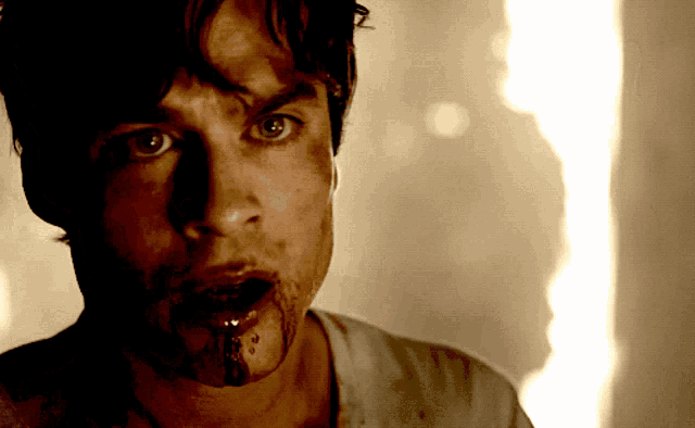 a man with blood coming out of his mouth looks at the camera