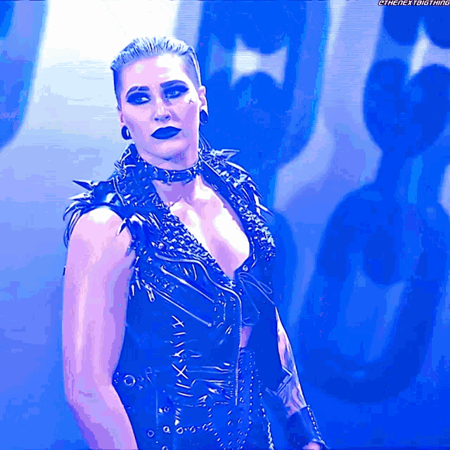 a woman wearing a black vest and choker stands in front of a blue background that says ' the next thing '