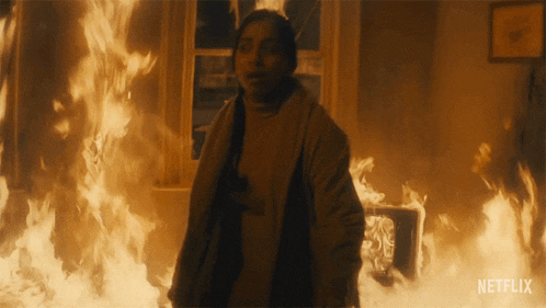 a woman is standing in front of a fire with netflix written on the bottom of the screen