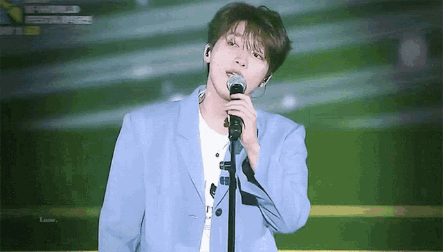 a man in a blue jacket is singing into a microphone on stage .