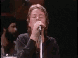 a man is singing into a microphone on a stage in a dark room .