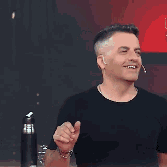 a man in a black t-shirt is smiling in front of a sign that says ' join '