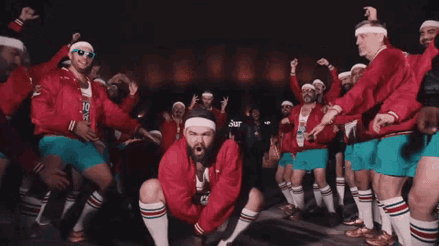 a man in a red jacket is surrounded by other men in blue shorts and socks