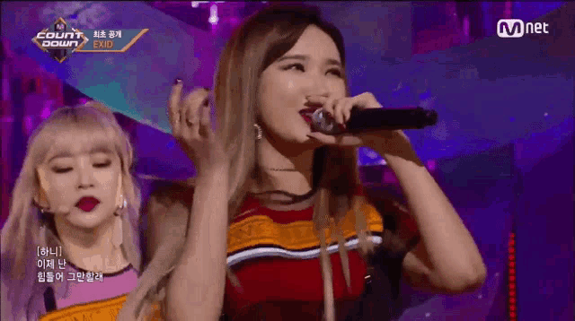 a woman singing into a microphone on a stage with a sign that says mnet
