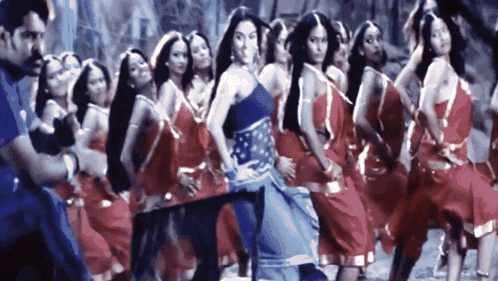 a woman in a blue dress is dancing in front of a group of women in red dresses