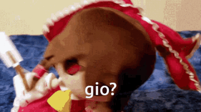 a stuffed animal in a red dress is laying on a bed and says gio ?
