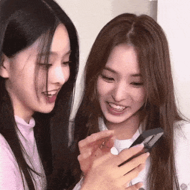 two women are looking at a cell phone and smiling