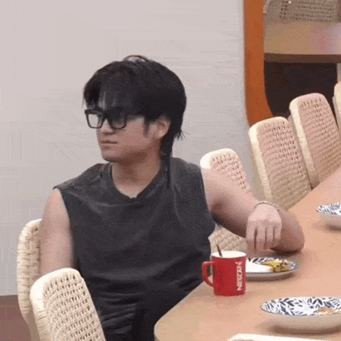 a man wearing glasses sits at a table with a red nescafe mug