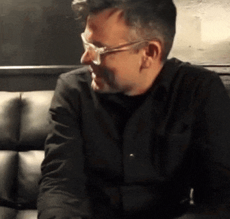 a man wearing glasses is sitting on a black couch