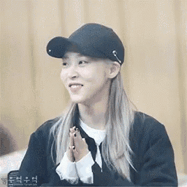 a woman wearing a black hat and a black jacket is smiling and holding her hands together .