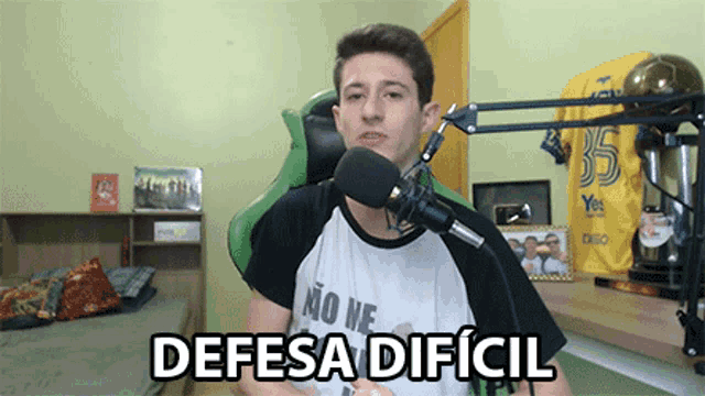 a man speaking into a microphone with the words " defesa dificil " written below him