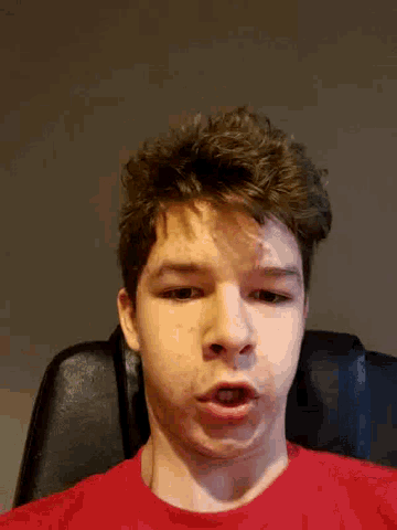 a young man in a red shirt is sitting in a chair