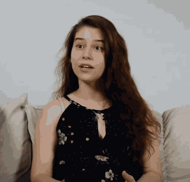 a woman sitting on a couch wearing a black floral dress