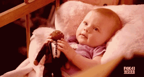 a baby is laying in a bed holding a stuffed animal .