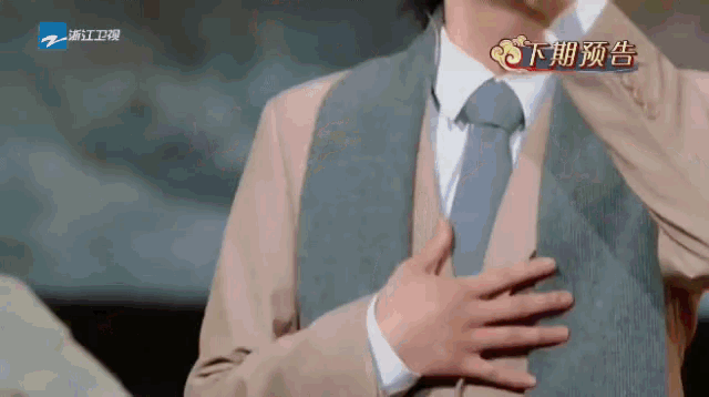 a man in a suit and tie has his hands on his chest in front of a sign that says ' a ' on it