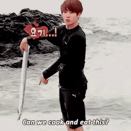 a young man is standing on the beach holding a long stick and asking can we cook and eat this