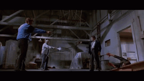 a man in a blue jacket is pointing a gun at a man in a black suit