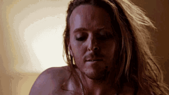 a shirtless man with long hair and a beard is laying on a bed .