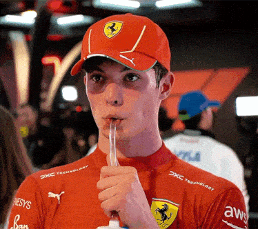 a man wearing a red ferrari hat is drinking something
