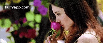 a woman is smelling a pink rose in front of flowers .