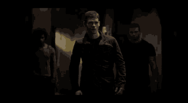 a man in a black shirt is walking down a dark hallway .
