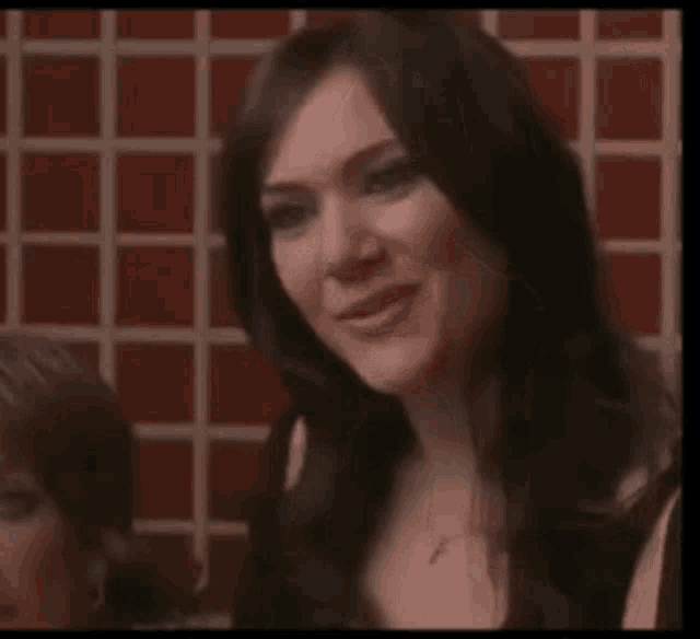 a woman with long dark hair is smiling in front of a red checkered wall .