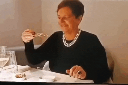 a woman wearing a pearl necklace is sitting at a table eating .