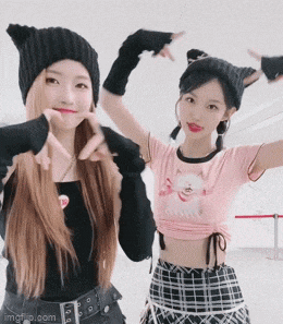 two girls are standing next to each other and making a heart with their hands .