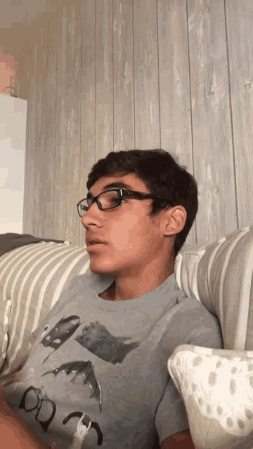 a young man wearing glasses and a batman t-shirt sits on a couch