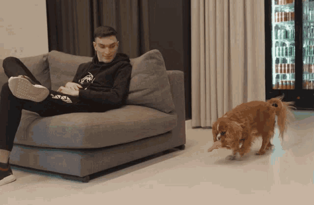 a man is sitting on a couch while a dog runs by