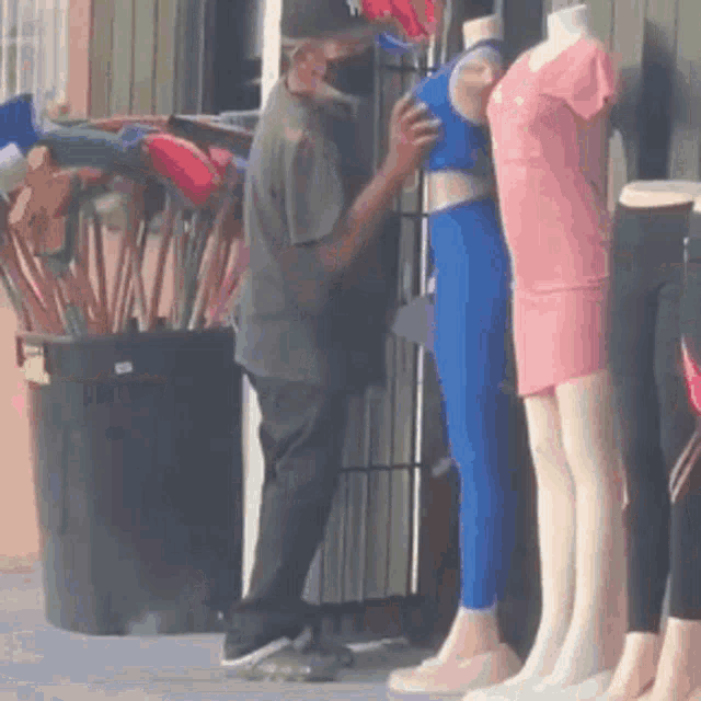 a man wearing a mask is touching a mannequin in front of a clothing store .