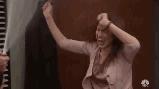 a woman is laughing and raising her arms in the air while holding a spray bottle .