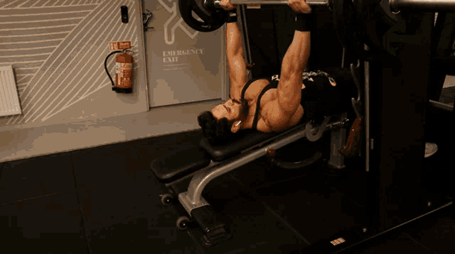 a man is lifting a barbell on a bench in front of an emergency exit
