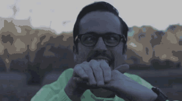 a man wearing glasses and a neon green sweater is biting his fingers .