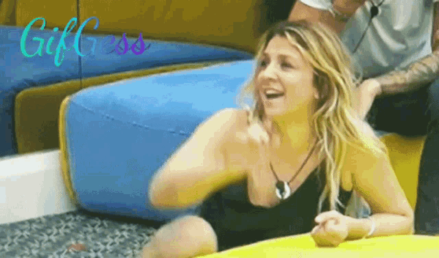 a woman in a black tank top is laying on a yellow cushion and smiling