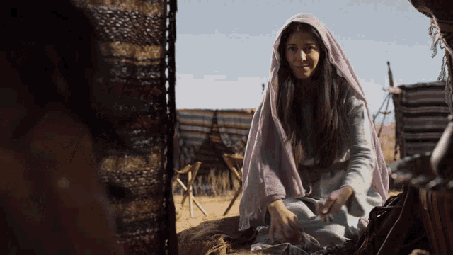 a woman wearing a purple veil sits in front of a tent