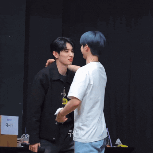 a man holding a microphone is hugging another man in front of a sign that says ' i love you '