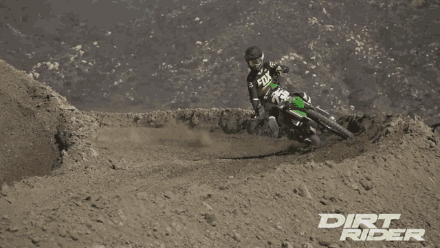 a dirt rider rides a green dirt bike on a dirt track